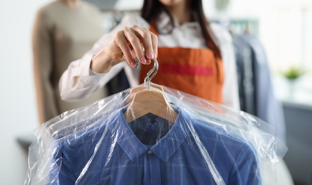 Administrator at dry cleaners keeps clean clothes on hangers in bag.