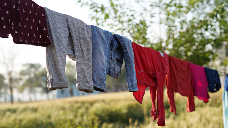 After being washed, Colorful clothing dries on a clothesline in the yard outside in the sunlight. Clothesline with freshly washed clothes outdoors in the morning