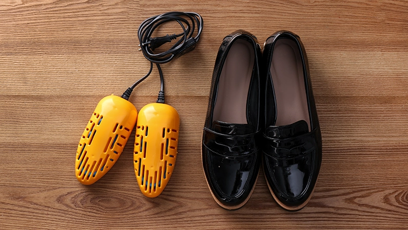 Shoes and electric dryer on wooden background, flat lay