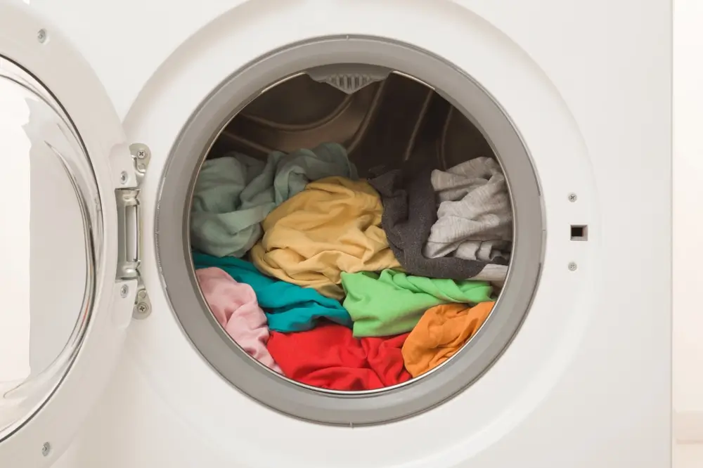 White opened washing machine full of colorful clothes.