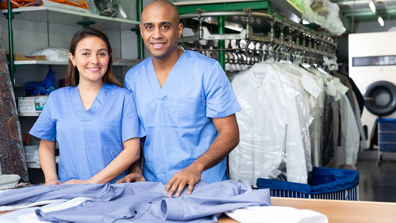 Two smiling workers offering professional dry cleaning, showing clean clothing
