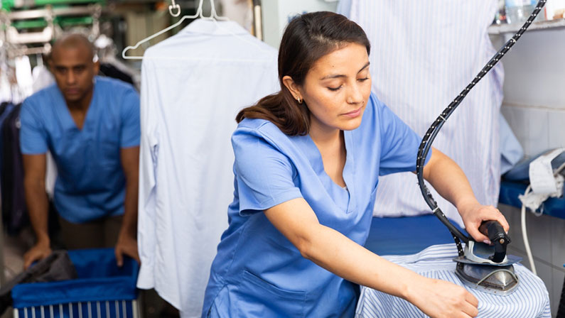 Focused woman laundry worker ironing shirt at dry-cleaning store