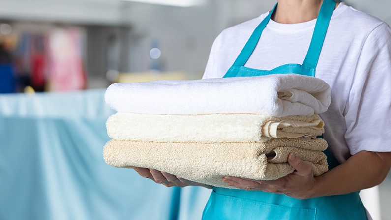 Cleaning woman in blue apron holding towels on blurred background.