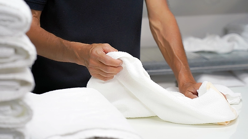 Hands of caucasian male laundry hotel worker folds a clean white towel. Hotel staff workers. Hotel linen cleaning services.