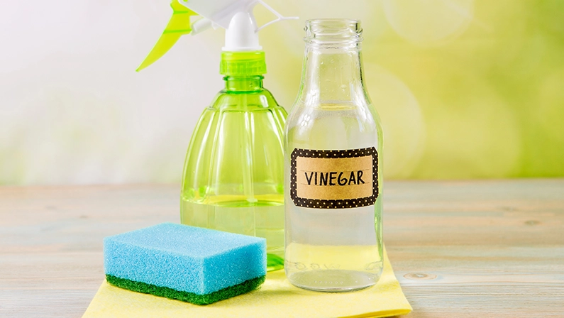 Chemical free home cleaner products concept. Using natural destilled white vinegar in spray bottle to remove stains. Tools on wooden table, green bokeh background, copy space.