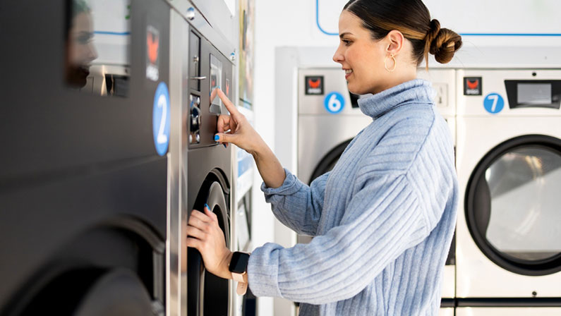 A pretty girl is inside a self-service laundry. The woman is choosing the washing program. Concept of public self-service washing machines.