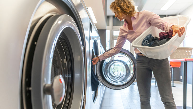 inserting dirty clothes into the washing machine in the laundry room