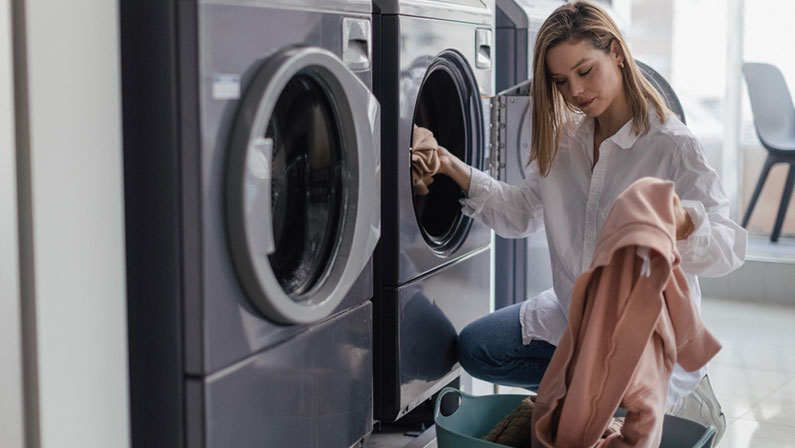 Young woman loading washing machine in public laundry.