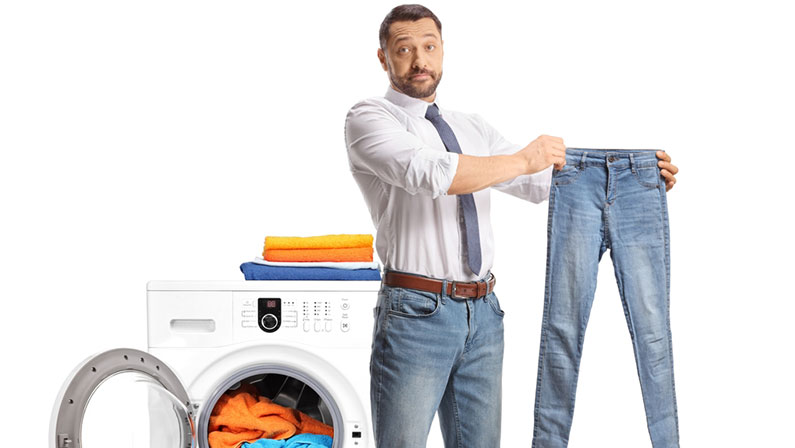 Man standing in front of a washing machine and holding a small pair of jeans isolated on white background