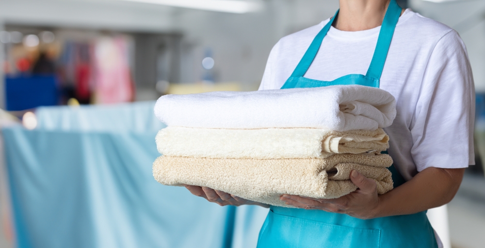 Cleaning woman in blue apron holding towels on blurred background.