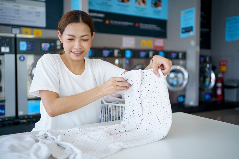 Happy Asian middle adult housewife is folding clothes on the table in the laundry shop