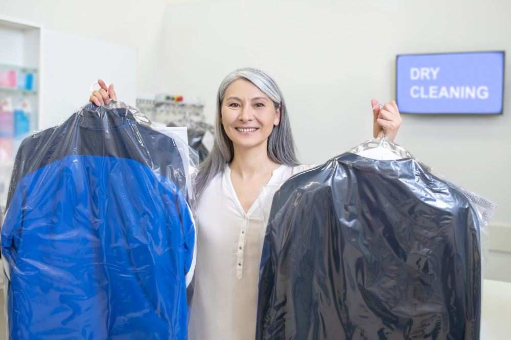 Happy pretty woman smiling standing in dry cleaning showing costumes packed in cases