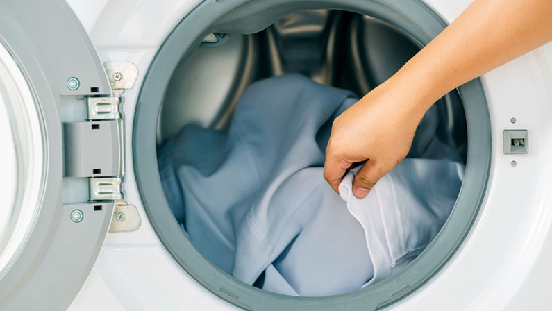 Close up man loading clothes into washing machine. Laundry concept.
