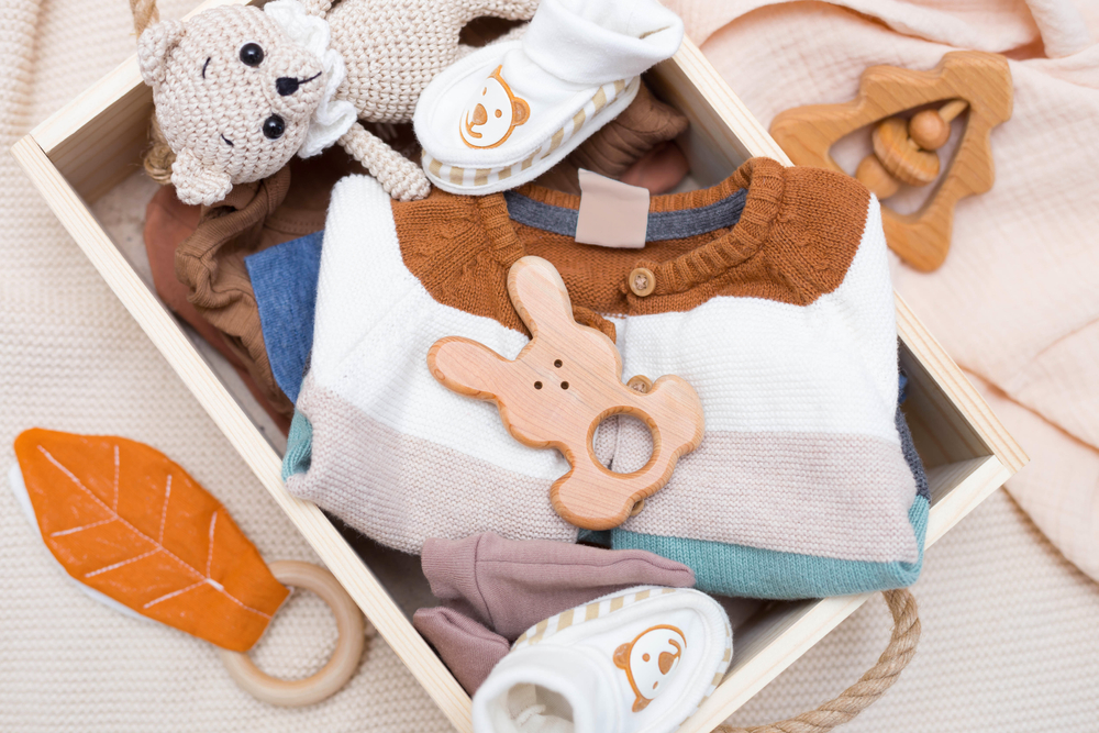 Newborn baby clothes and wooden toys in a box on a light background.