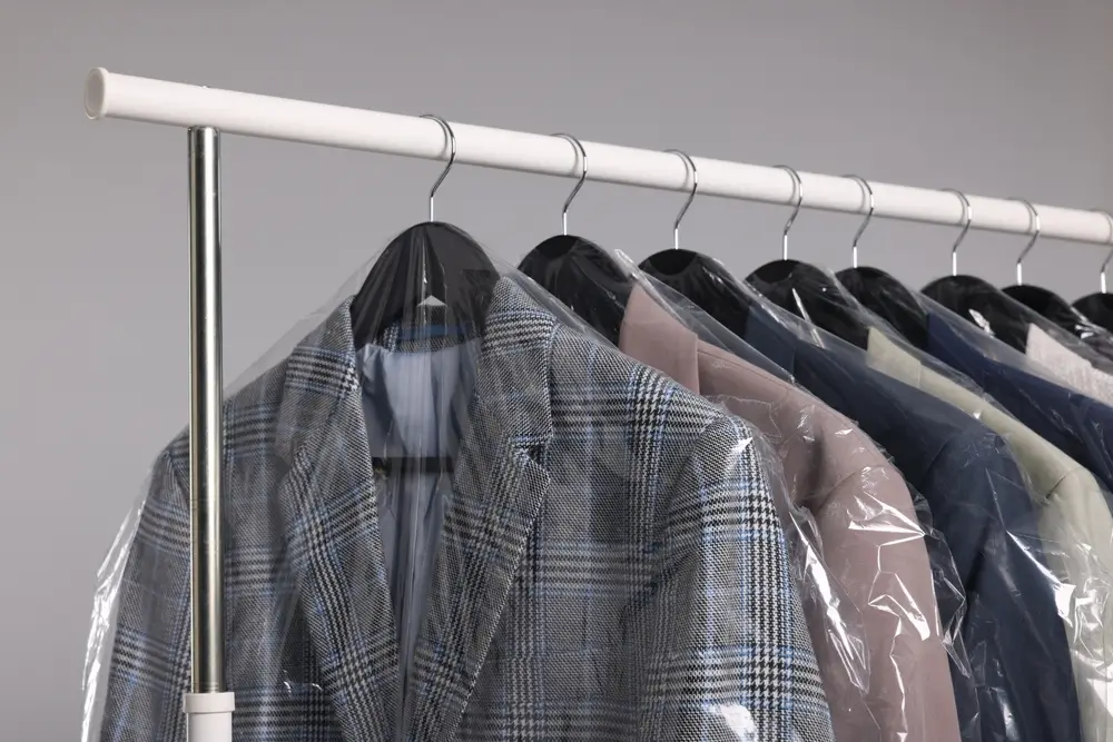 Many different clothes in plastic bags hanging on rack against grey background