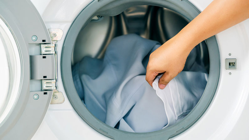 Close up man loading clothes into washing machine.