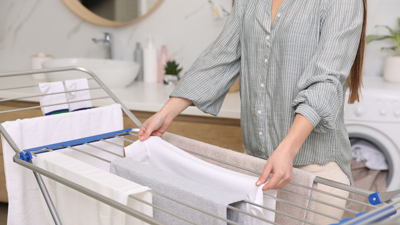 Young woman hanging clean laundry on drying rack in bathroom, closeup
