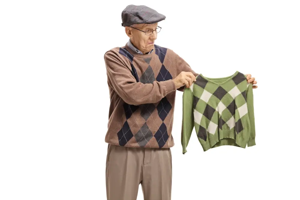 Disappointed elderly man looking at a shrunken sweater isolated on white background
