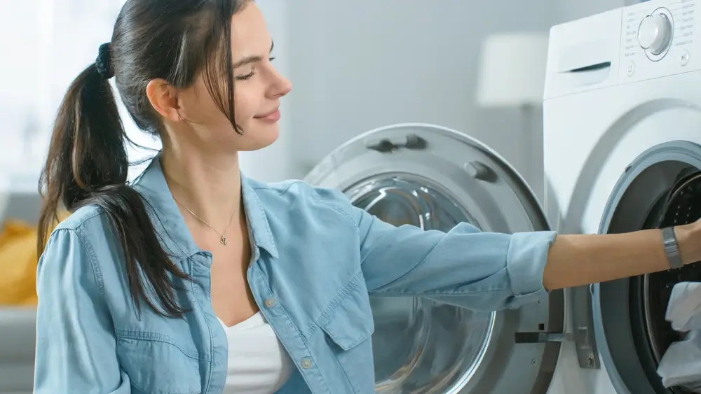 Close Up Shot of a Beautiful Young Woman in Homely Clothes Sitting in Front of a Washing Machine.