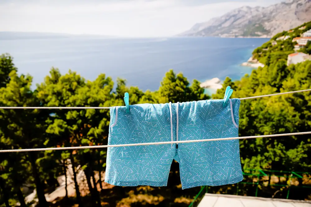 Blue men's swim shorts hanging on the clothesline on the sea and mountains background
