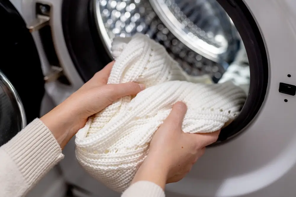 Woman putting white clothes into the drum of a washing machine, front view. 