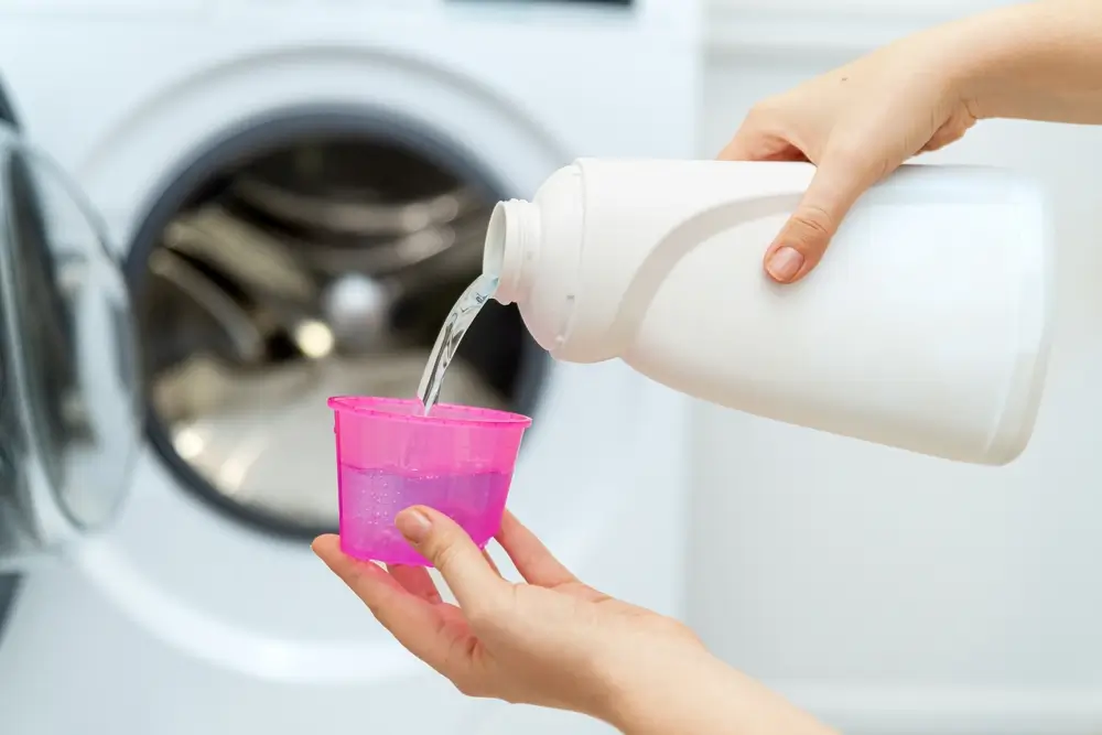 Person adding liquid laundry detergent to the washer, close up. 