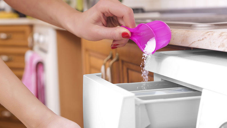 Woman throws laundry detergent into the washing machine close-up.
