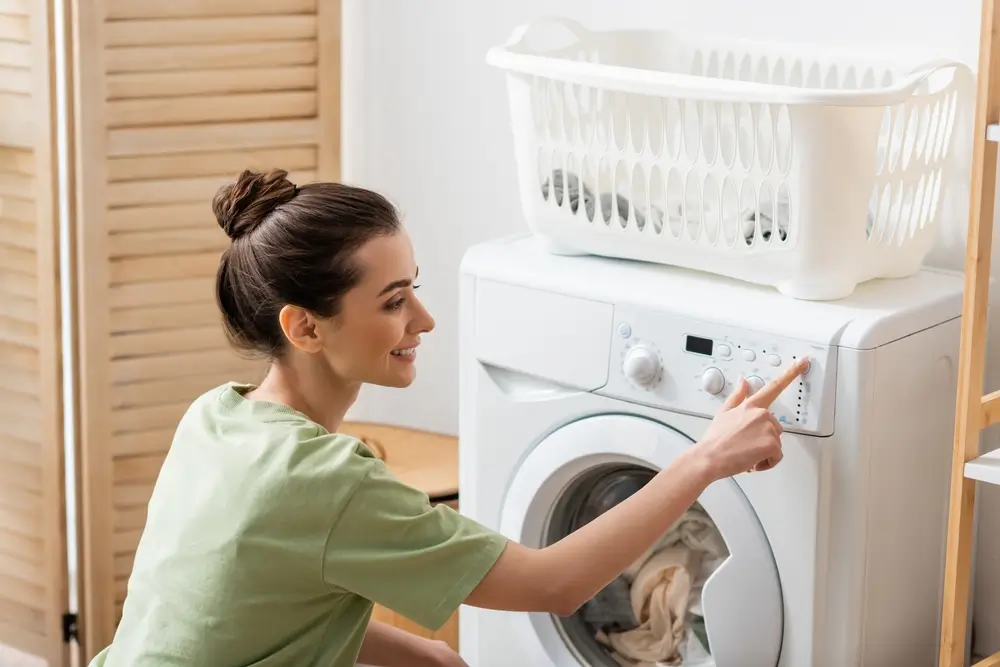 Side view of young woman switching washing machine at home
