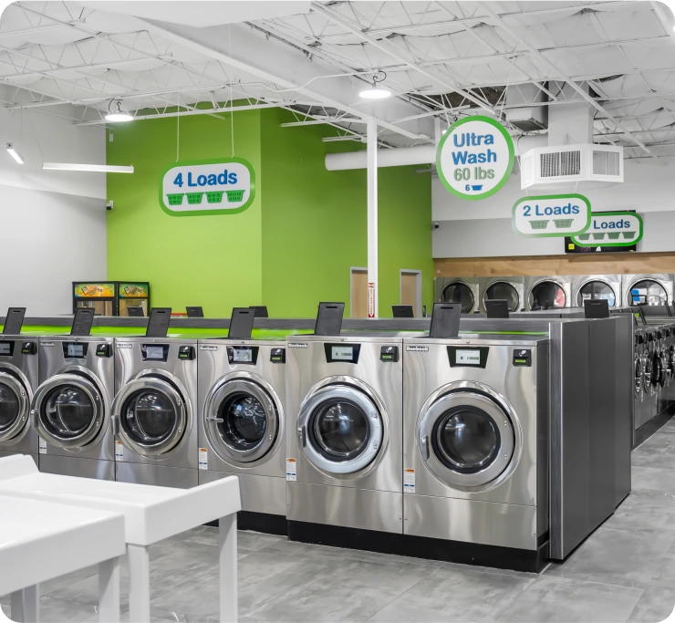 A row of bright and colorful commercial washing machines in various sizes at a clean laundromat.