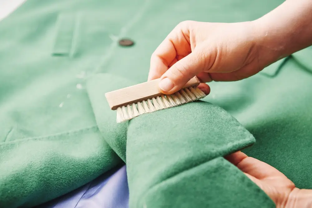 Female hand cleans coat fabric with a small brush.