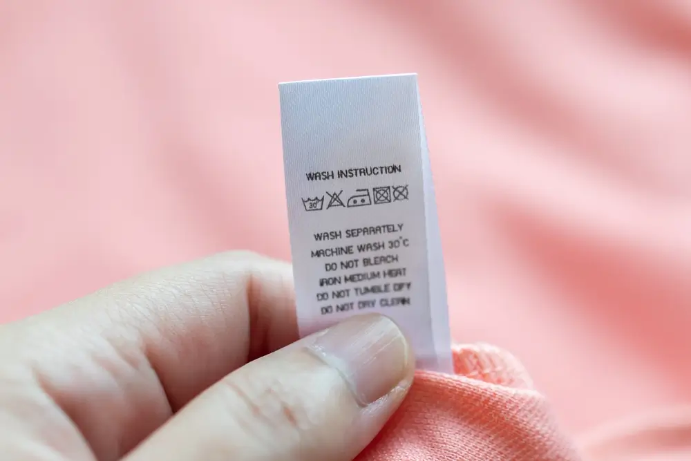 Hand hold and reading at white laundry care washing instructions clothes label on pink shirt