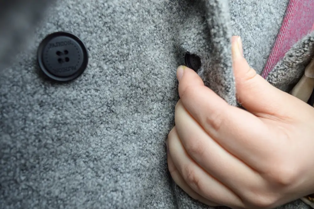 close-up view of a hand fastening a button on a textured gray wool coat