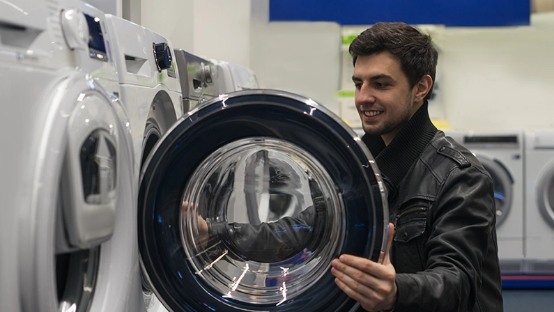 portrait of male customer choosing washer in supermarket store. He opened washing machine cover