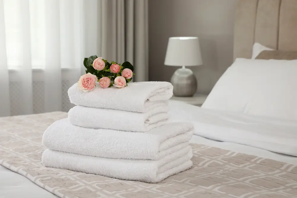 Freshly folded white towels stacked on a bed with roses, showcasing the quality results of professional drop-off services.