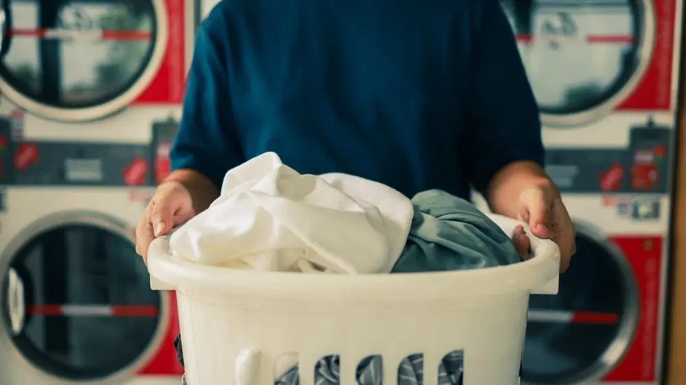 A person holding a laundry basket filled with clothes at a laundromat, using convenient drop-off services for hassle-free cleaning.