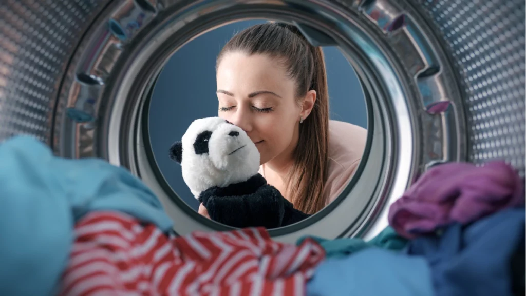 Smiling woman washing a panda plush in the washing machine, point of view shot