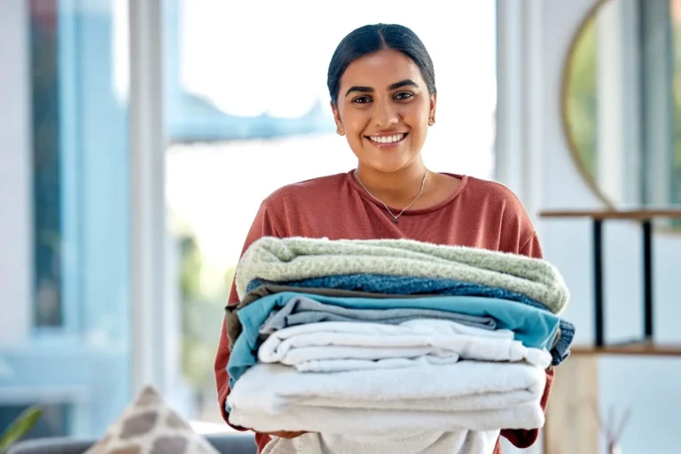 woman holding pile of laundry and smiling at camera