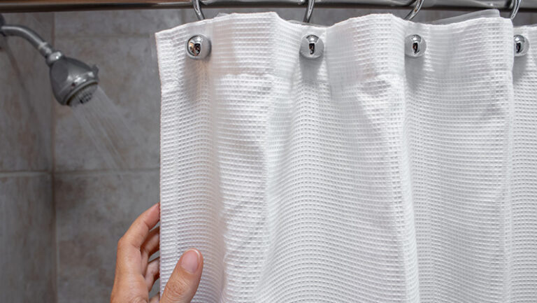 a hand pulling back a shower curtain revealing a shower head with water on horizontal shot