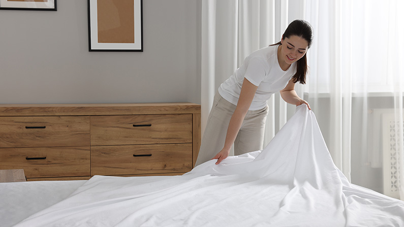Young woman changing bed linens at home