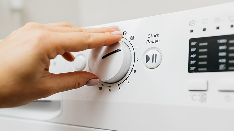 A woman loads dirty laundry into the washing machine and sets the wash cycle. Concept: caring for cleanliness and comfort at home, simplifying daily life with modern technology.