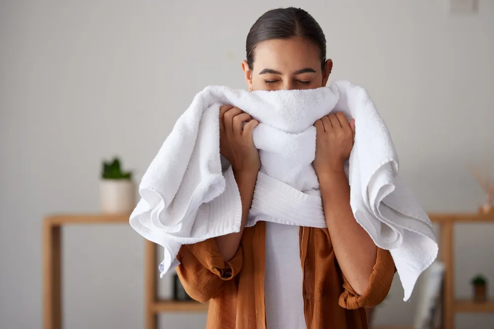 Laundry, fresh and woman smelling a towel after cleaning, housework and washing clothes in the morning
