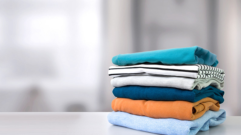 Stack of colorful clothes. Pile of clothing on table empty space background. Laundry and household.