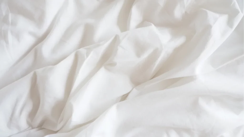 Closeup of beautiful white shiny crumpled polyester fabric sheets on the bed with warm motion and feeling for background and decoration