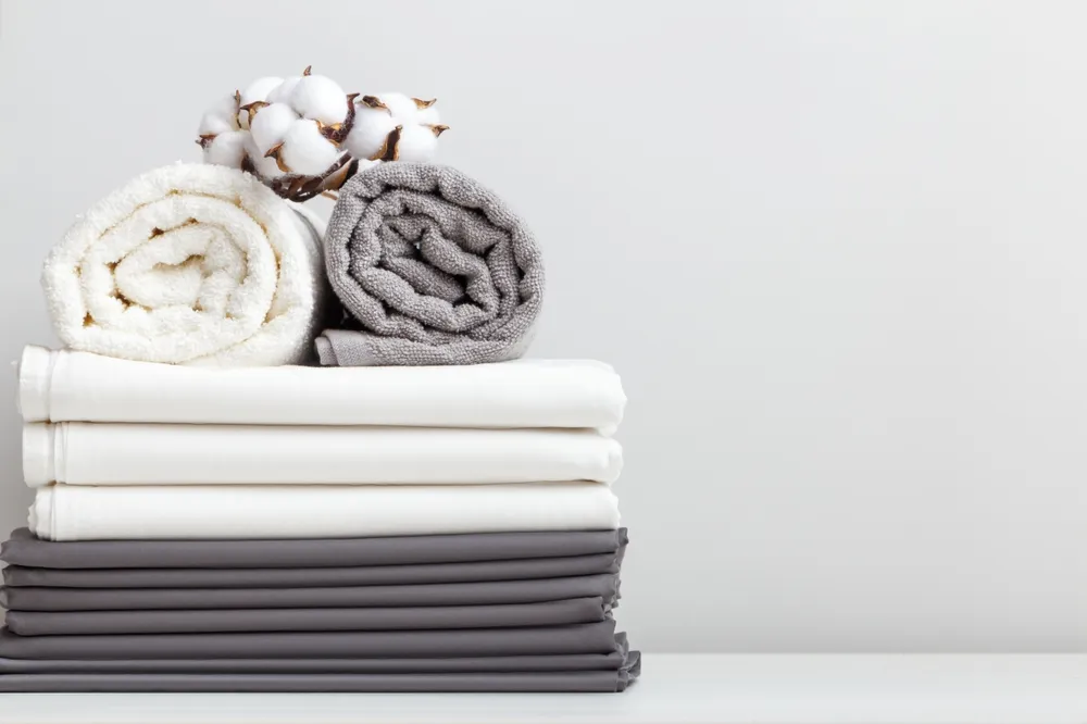 Gray white bed linen, a sheet and two rolled up towels on the table.