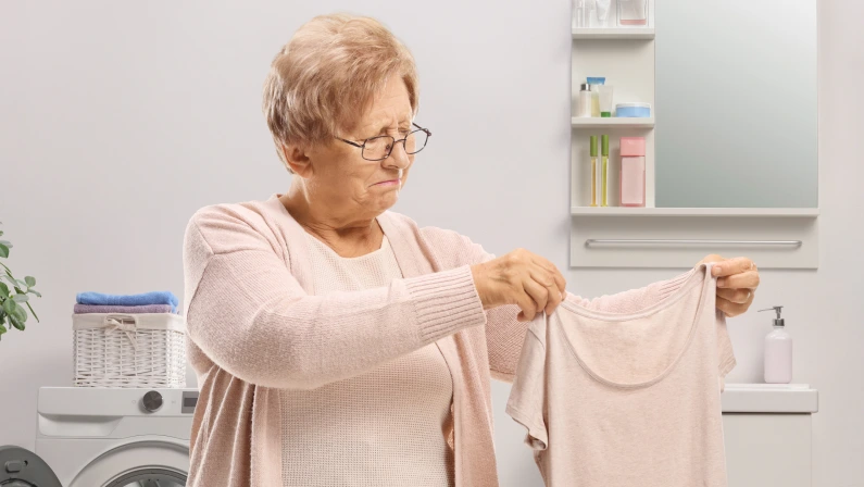Elderly woman holding a shrunken t-shirt inside a bathroom with a washing machine