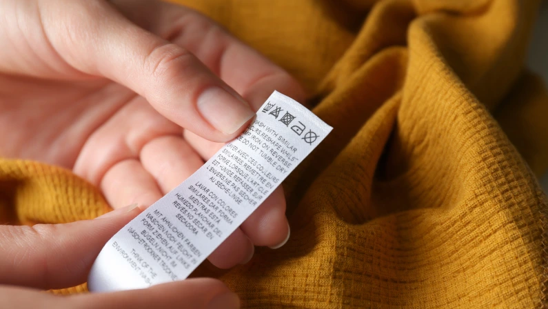 Woman reading clothing label with care instructions on yellow garment, closeup