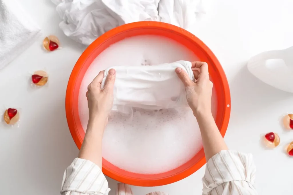 closeup of person hand washing clothes in an orange bucket