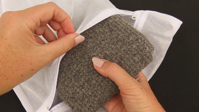 Woman hands putting a folded gray clothing to wash into a laundry bag on black background.