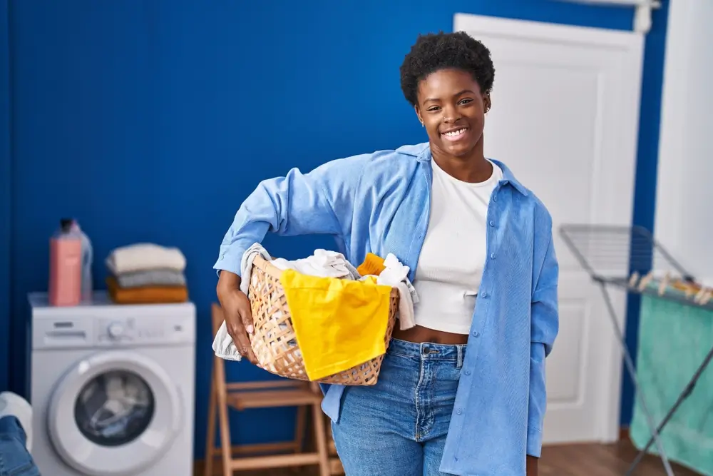African american woman holding laundry basket looking positive and happy standing and smiling with a confident smile showing teeth
