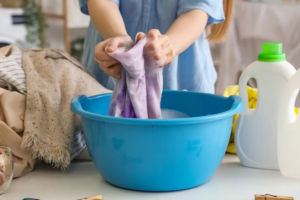 Woman washing clothes in plastic basin on white table